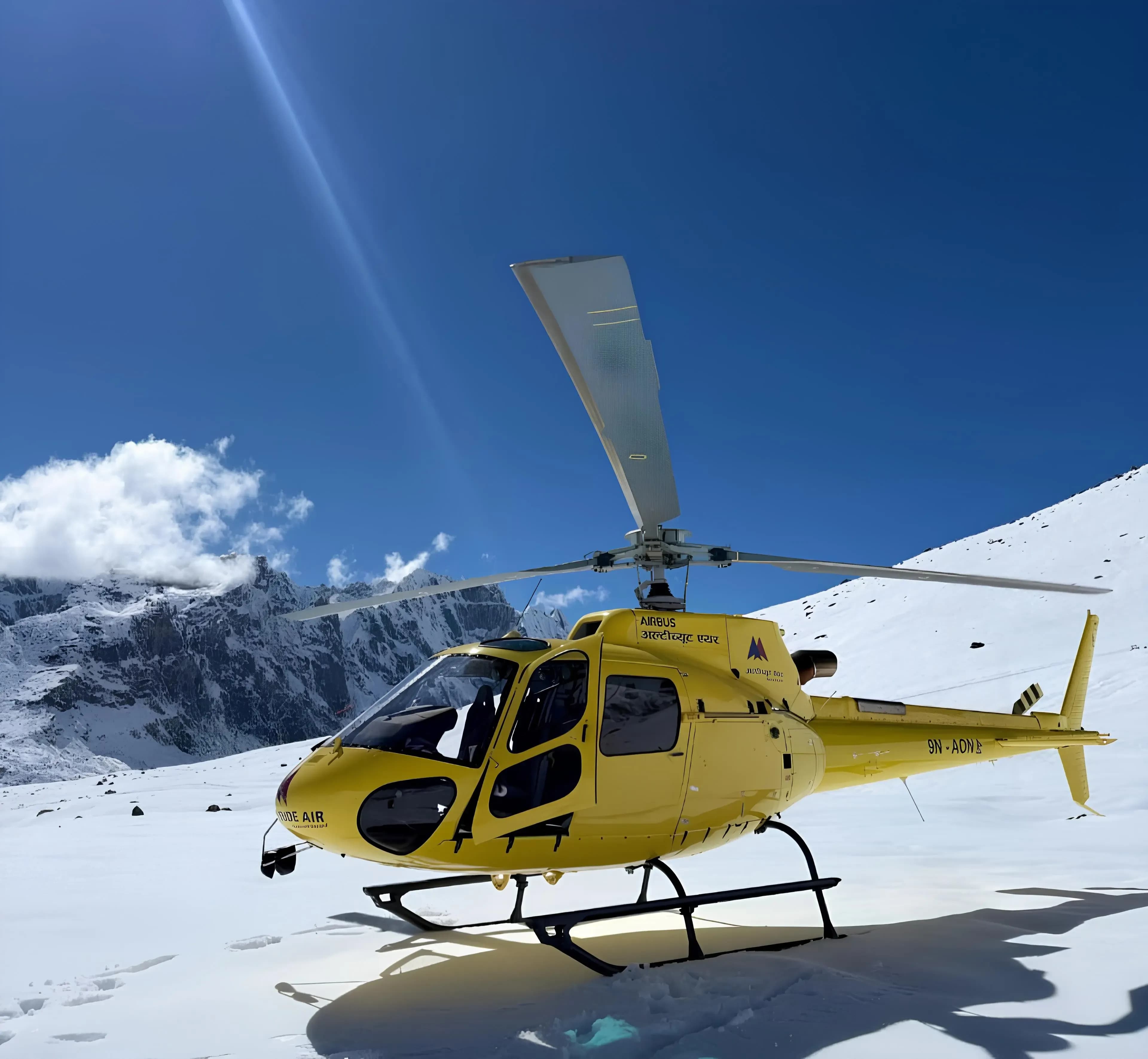 Altitude Air yellow helicopter landed on deep snow in the Everest region of Nepal with Himalayan mountains in the background.